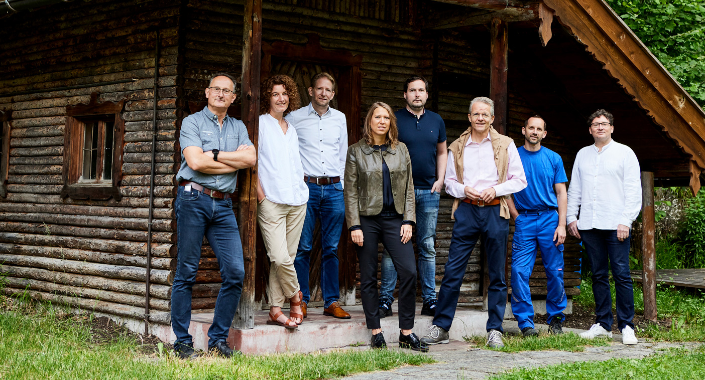 Women and men standing in front of a little wooden hut