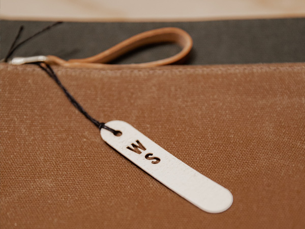 Weißes plastikfreies Hangtag aus Papier mit ausgestanzten Buchstaben W und S welches mit einem schwarzen Faden an einer Tasche befestigt ist