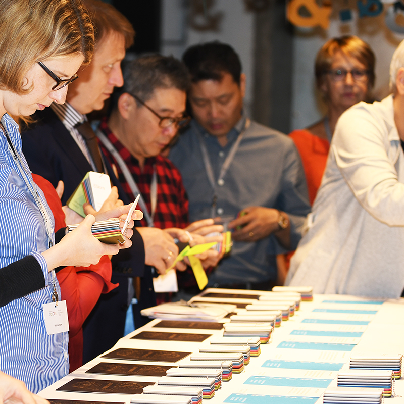 Männer und Frauen die an einem Papierworkshop teilnehmen und nachhaltige Papier sichten und fühlen